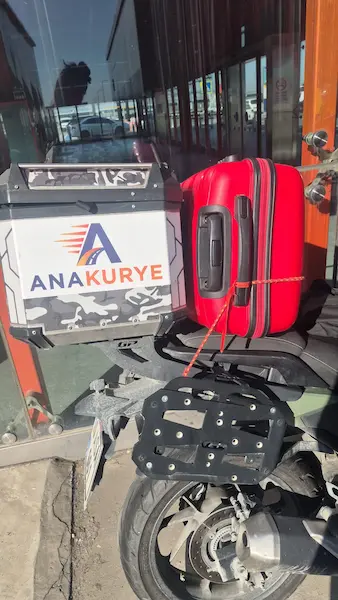 Red suitcase secured beside the Ana Kurye courier box during preparation